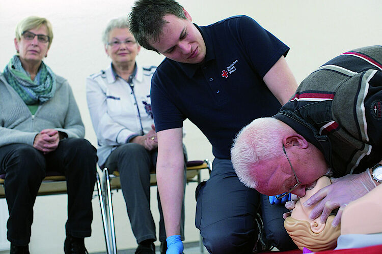 Ein älterer Mann übt an einer Puppe Mund zu Mund Beatmung