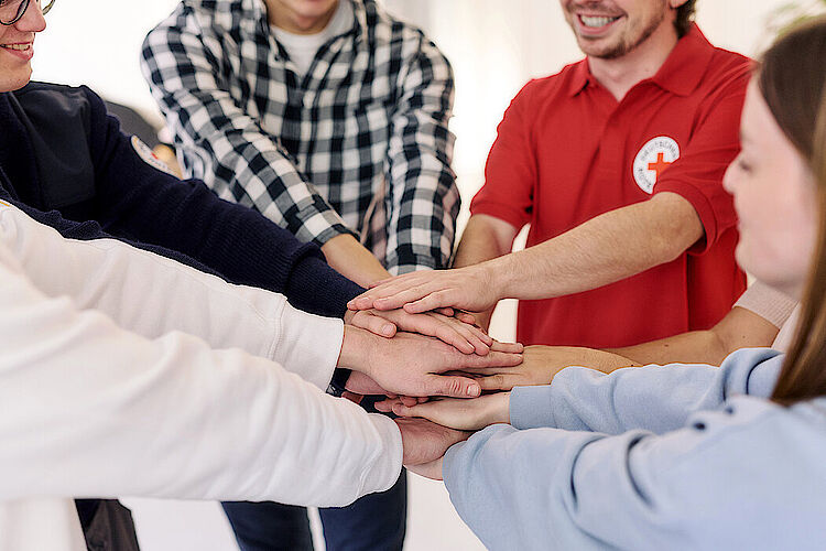 Mehrere Menschen haben sich in einem Kreis aufgestellt und halten ihre Hände übereinander