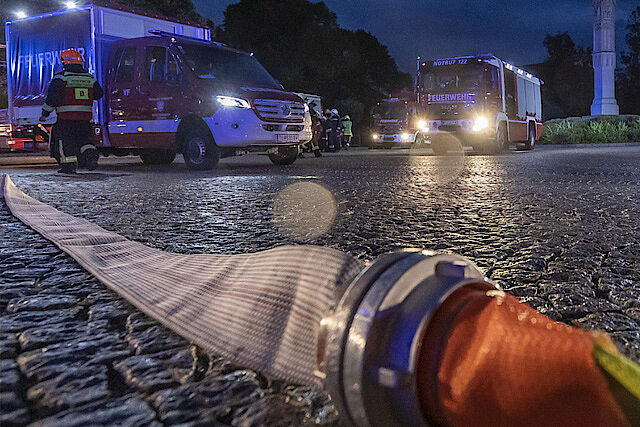 Feuerwehrschlauch im Vordergrund, im Hintergrund Rettungsfahrzeuge
