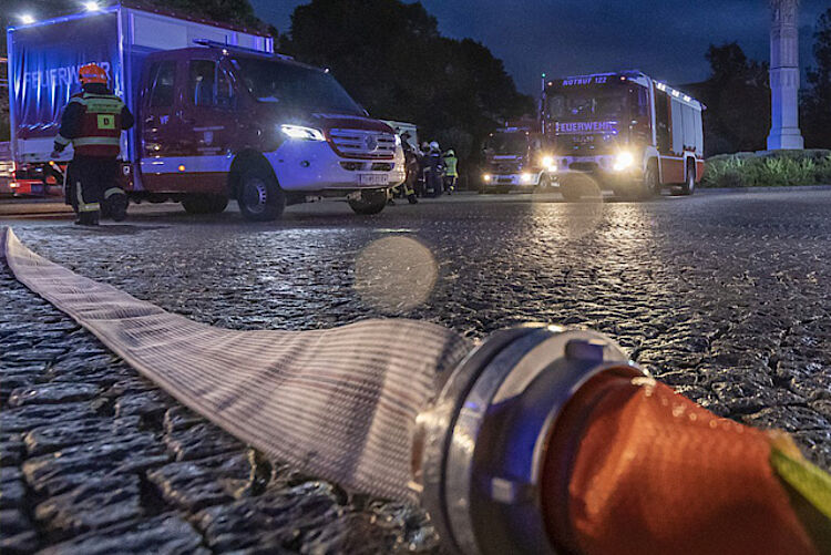 Feuerwehrschlauch im Vordergrund, im Hintergrund Einsatzfahrzeuge