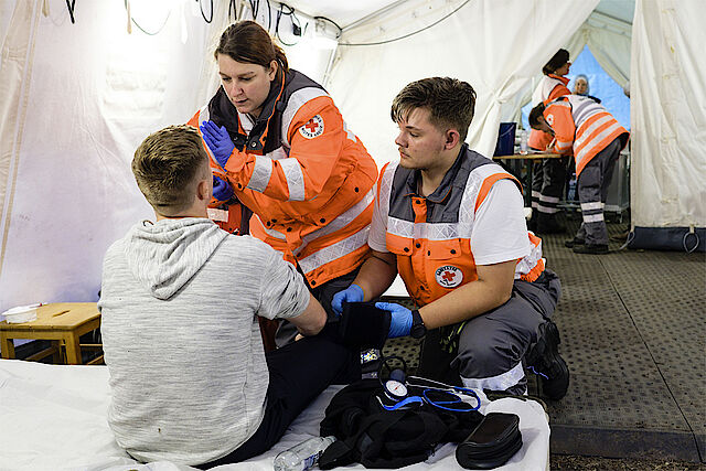 DRK-Mitarbeiter des Sanitätsdienstes versorgen einen Verletzten in einem Zelt