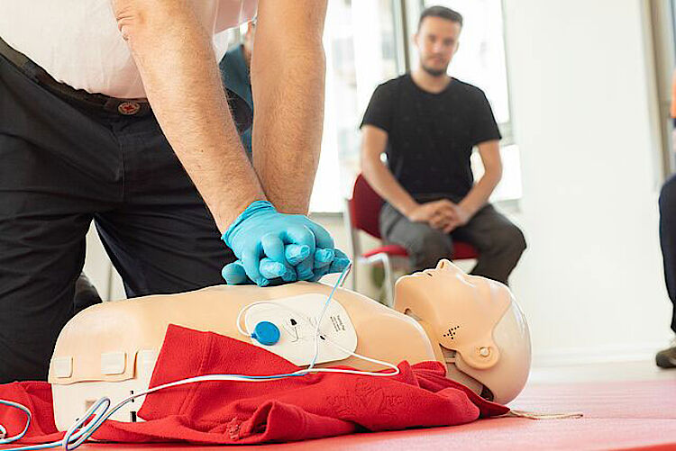 Jemand zeigt in einem Kurs Herzmassage mit Defibrillator