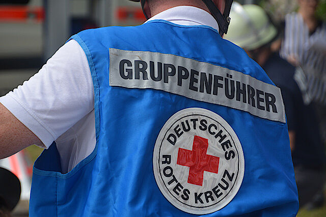 Rücken eines DRK-Mitarbeiters mit blauer Weste, auf der DRK Logo und das Wort Gruppenführer steht